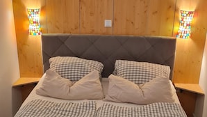 Een bed met een houten hoofdbord, geruit beddengoed en twee wandlampen.