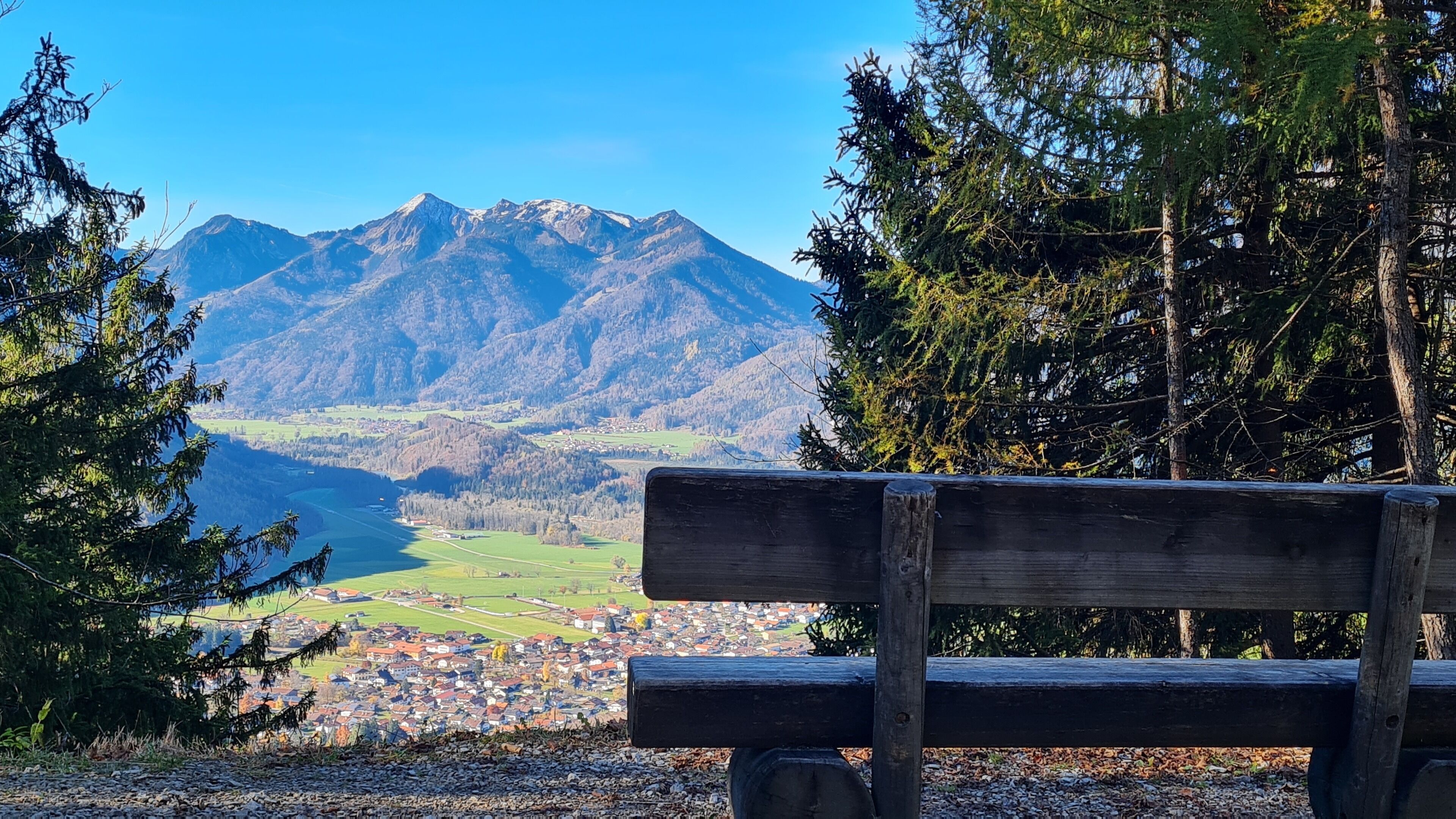 Um banco de madeira com vista para uma paisagem montanhosa e uma aldeia lá embaixo.