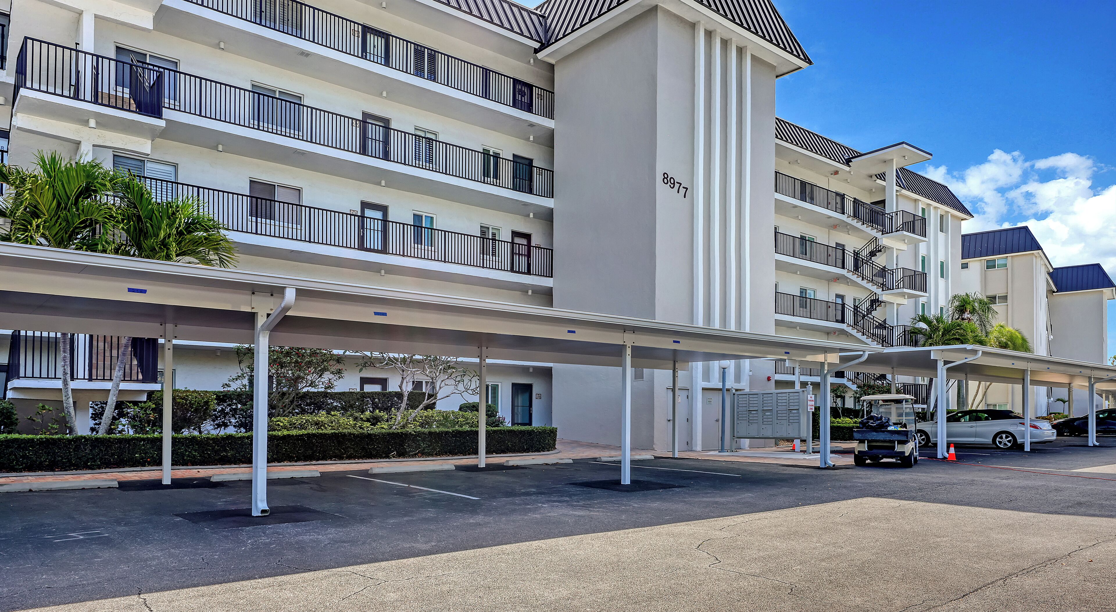 A multi-story hotel with balconies, a covered parking area, and a clear sky.