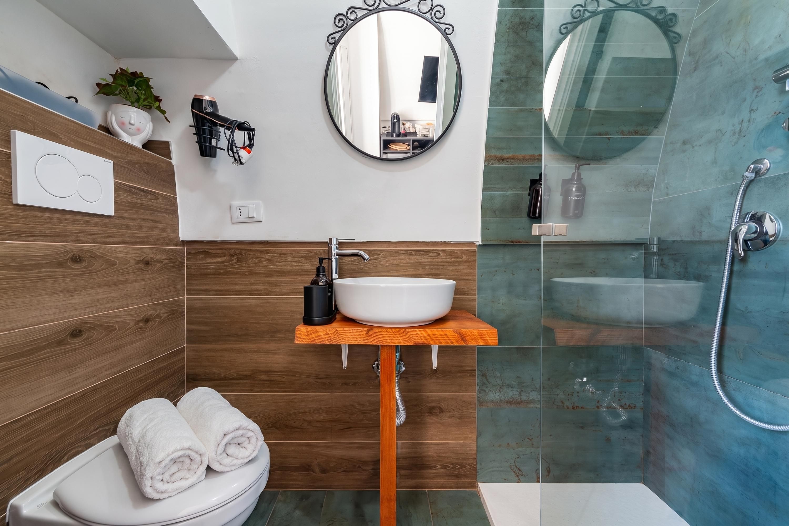 A modern bathroom with a wooden vanity, a white sink, a mirror, and a glass-enclosed shower.