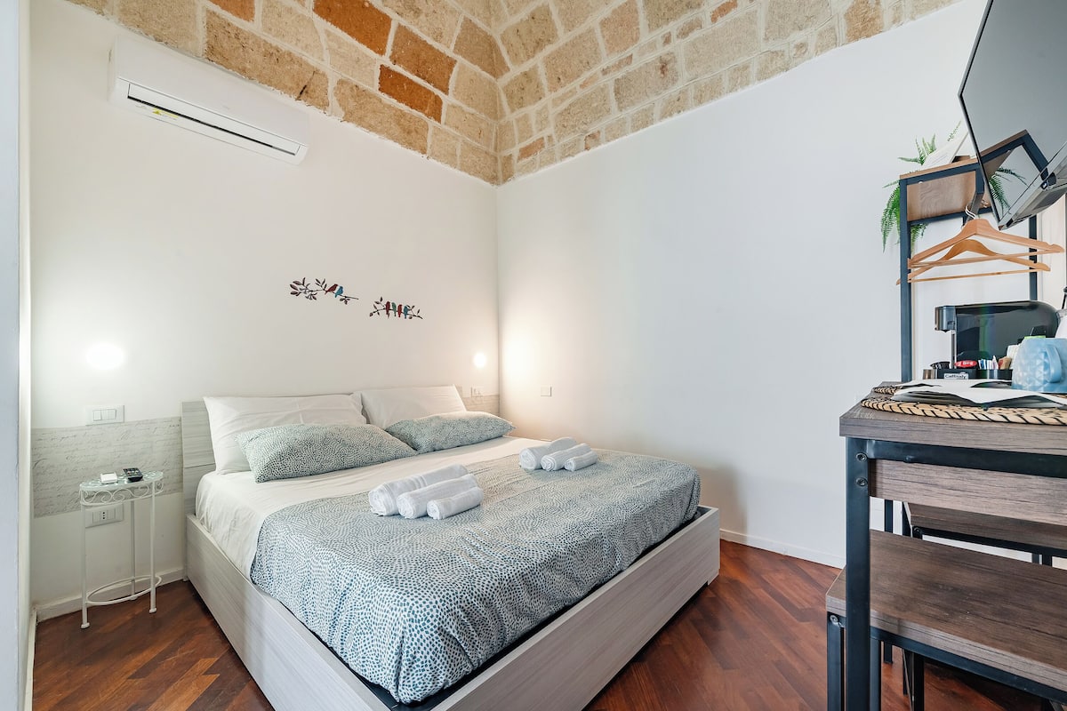Un dormitorio con cama, mesita de noche y escritorio con silla.