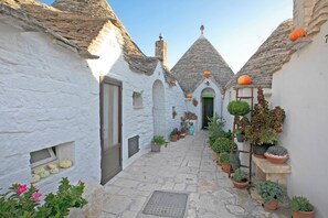 A narrow cobblestone alley flanked by white buildings with stone roofs, potted plants, and a small door. - Tresor Rooms (Polignano a Mare)