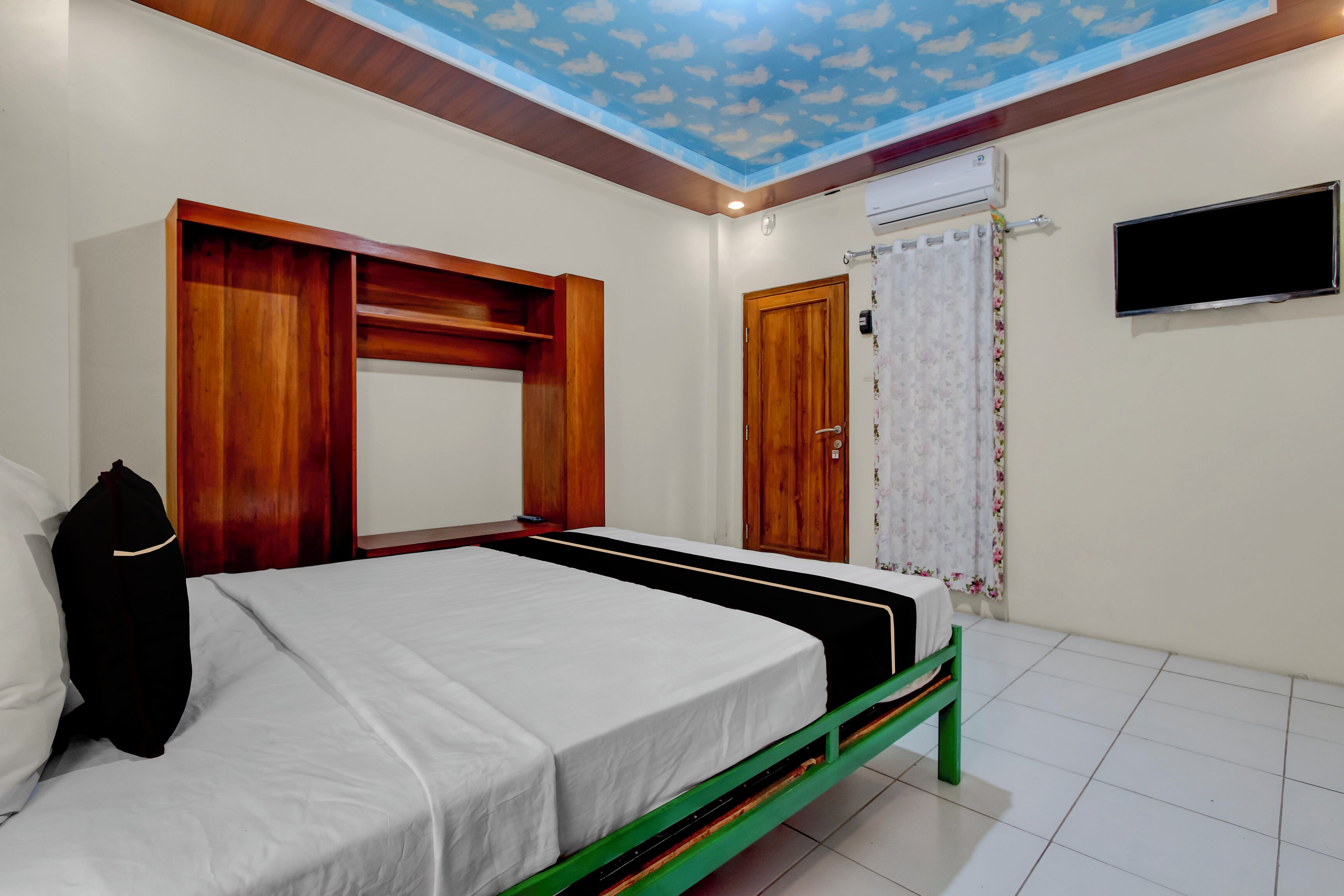 Un dormitorio con cama, armario de madera y televisor en la pared.
