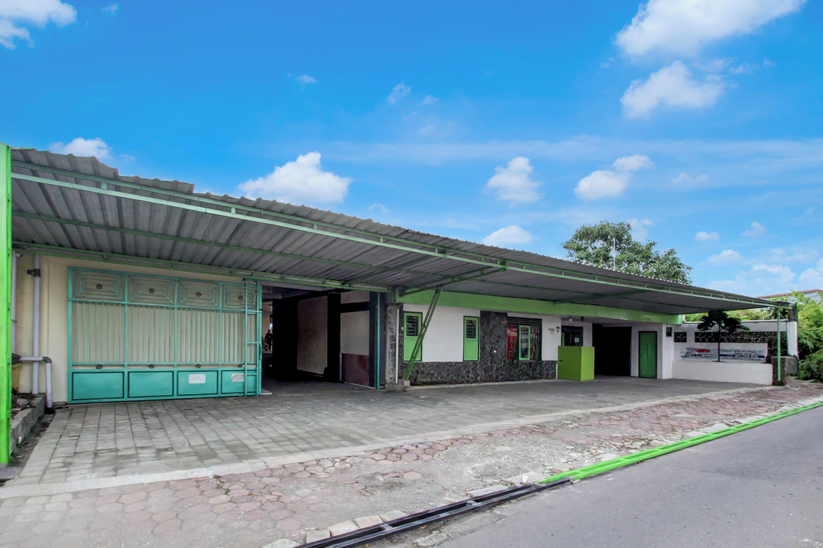 A building with a green and white facade, a covered entrance, and a paved area in front.