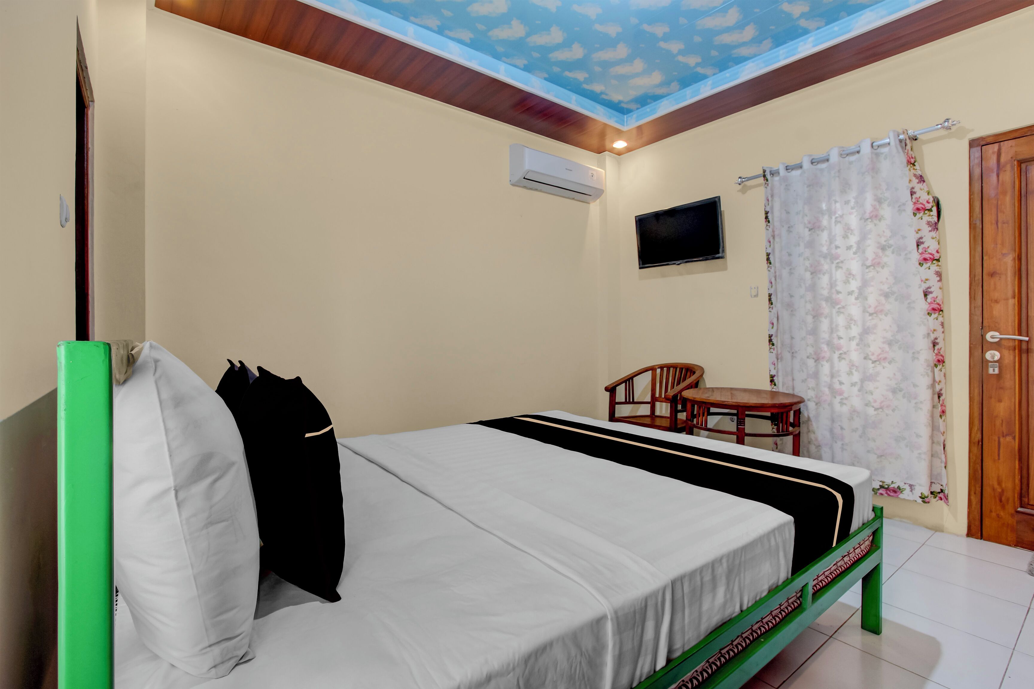 A bedroom with a bed, a television, a wooden chair, and a small table.