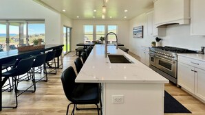 A modern kitchen with a large island, white cabinetry, and a view of the outdoors. - Luxury Home at Bear Lake! Sleeps 30! Resort Hot Tub! Tesla Charging! (Fish Haven)