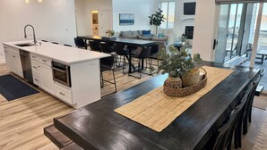 A modern kitchen with a central island, dining area with chairs, and a large window offering a view of the outdoors. - Luxury Home at Bear Lake! Sleeps 30! Resort Hot Tub! Tesla Charging! (Fish Haven)