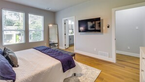 A bedroom with a bed, a ceiling fan, a TV mounted on the wall, and a door leading to a bathroom. - Luxury Rooftop Retreat - Near AT&T & Six Flags (Arlington)