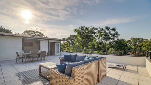 A rooftop patio with a wicker sofa, a dining table, and chairs. - Luxury Rooftop Retreat - Near AT&T & Six Flags (Arlington)