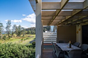 Eine überdachte Terrasse mit Tisch und Stühlen, mit Blick auf einen angelegten Garten und ferne Hügel.