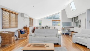 Ein großzügiger Wohnbereich mit weißem Sofa, Korbstühlen, einem Holztisch und einer Küche im Hintergrund.