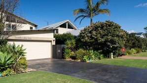 Ein modernes, zweistöckiges Haus mit Garage, umgeben von gepflegten Rasenflächen und tropischen Pflanzen.