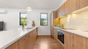 A modern kitchen with wooden cabinets, a white countertop, a built-in oven, and two windows providing natural light. - Byron Bay Accom - Keesing Villa 8 right in the heart of Byron Bay (Byron Bay)
