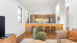 A modern kitchen with wooden cabinets, a central island with stools, and a built-in oven. - Byron Bay Accom - Keesing Villa 8 right in the heart of Byron Bay (Byron Bay)