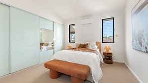 A bedroom with a bed, a bench, a mirror, two bedside tables, and a window. - Byron Bay Accom - Keesing Villa 8 right in the heart of Byron Bay (Byron Bay)