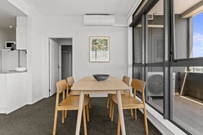 Ett modernt matområde med ett stort bord och sex stolar, ett vitt kök med mikrovågsugn och ett stort fönster med utsikt över omgivningen.