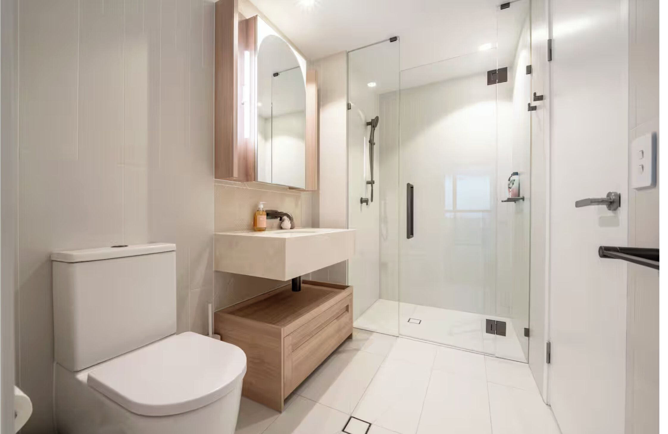A modern bathroom with a toilet, vanity, and glass shower enclosure.
