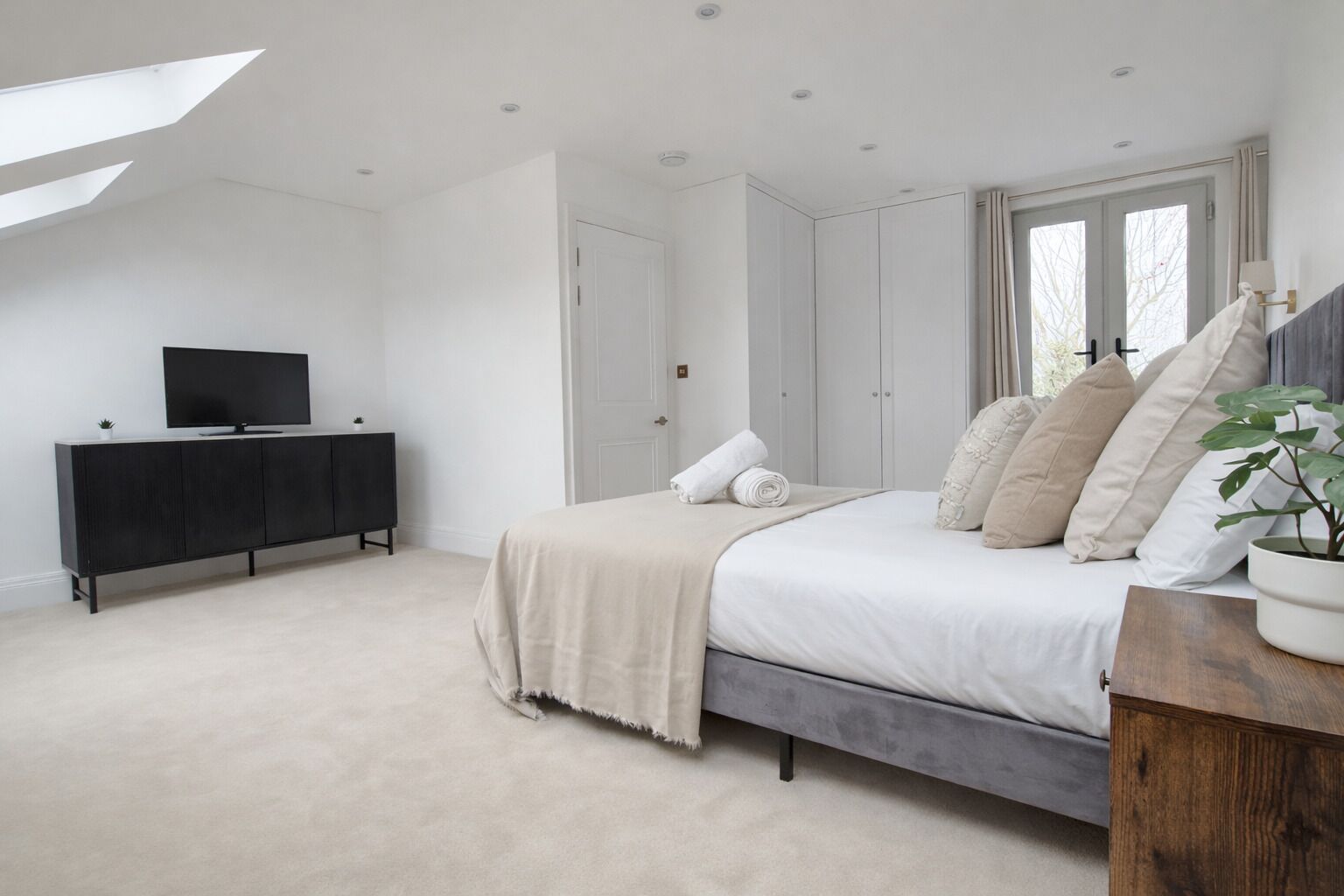 A bedroom with a bed, a TV on a cabinet, and a window with curtains.