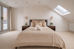 A bedroom with a large bed, two bedside tables, a skylight, and a view of the outside. - Beautiful Five-Bedroom House  (London)