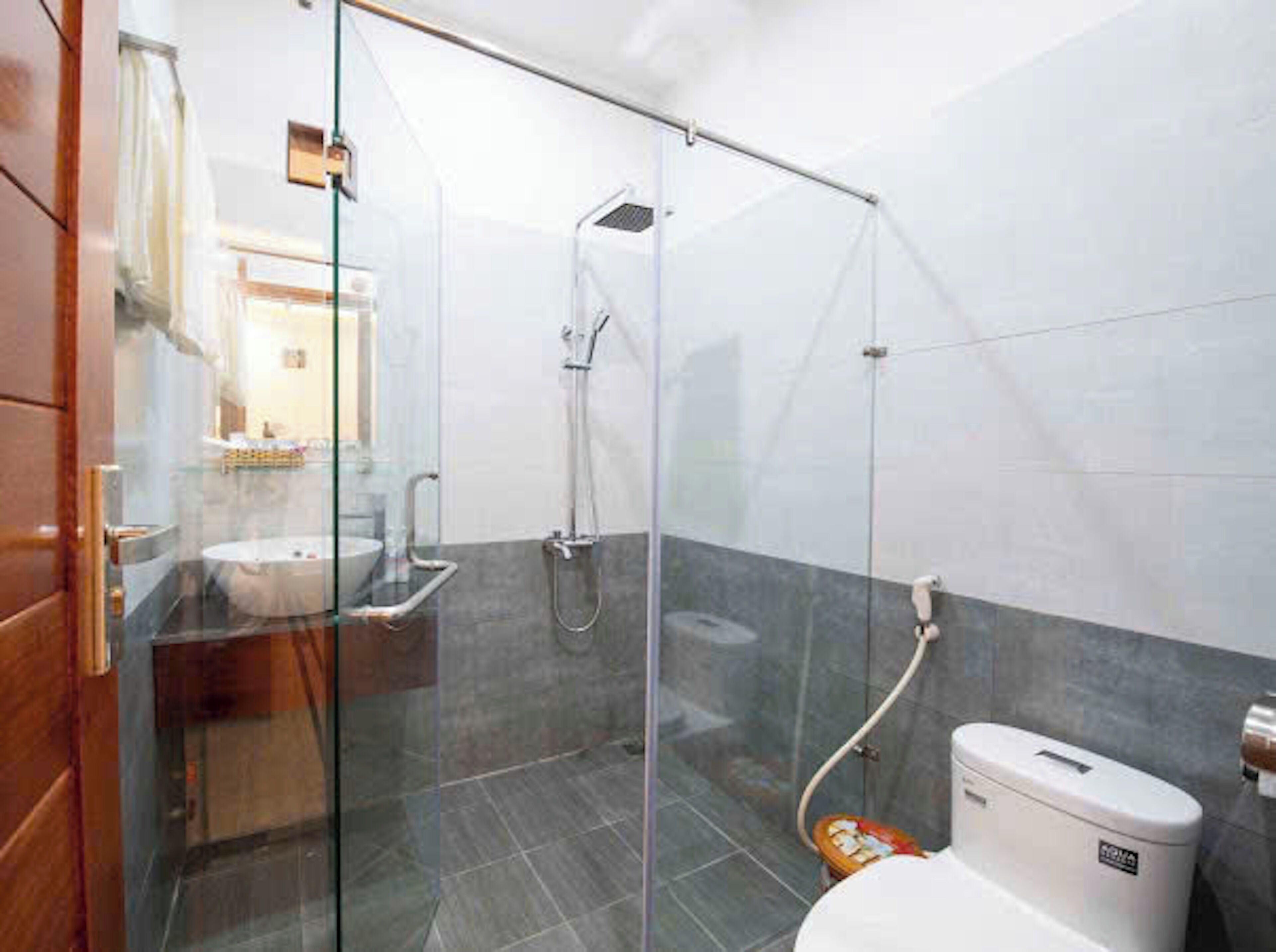 Un baño moderno con cabina de ducha de vidrio, un lavabo blanco y un inodoro.