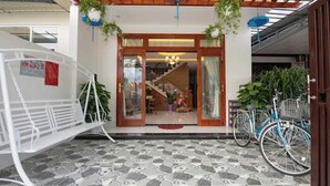 A building entrance with a tiled floor, a wooden pergola, hanging plants, and bicycles. - Hoi An Impression Homestay (Hoi An)