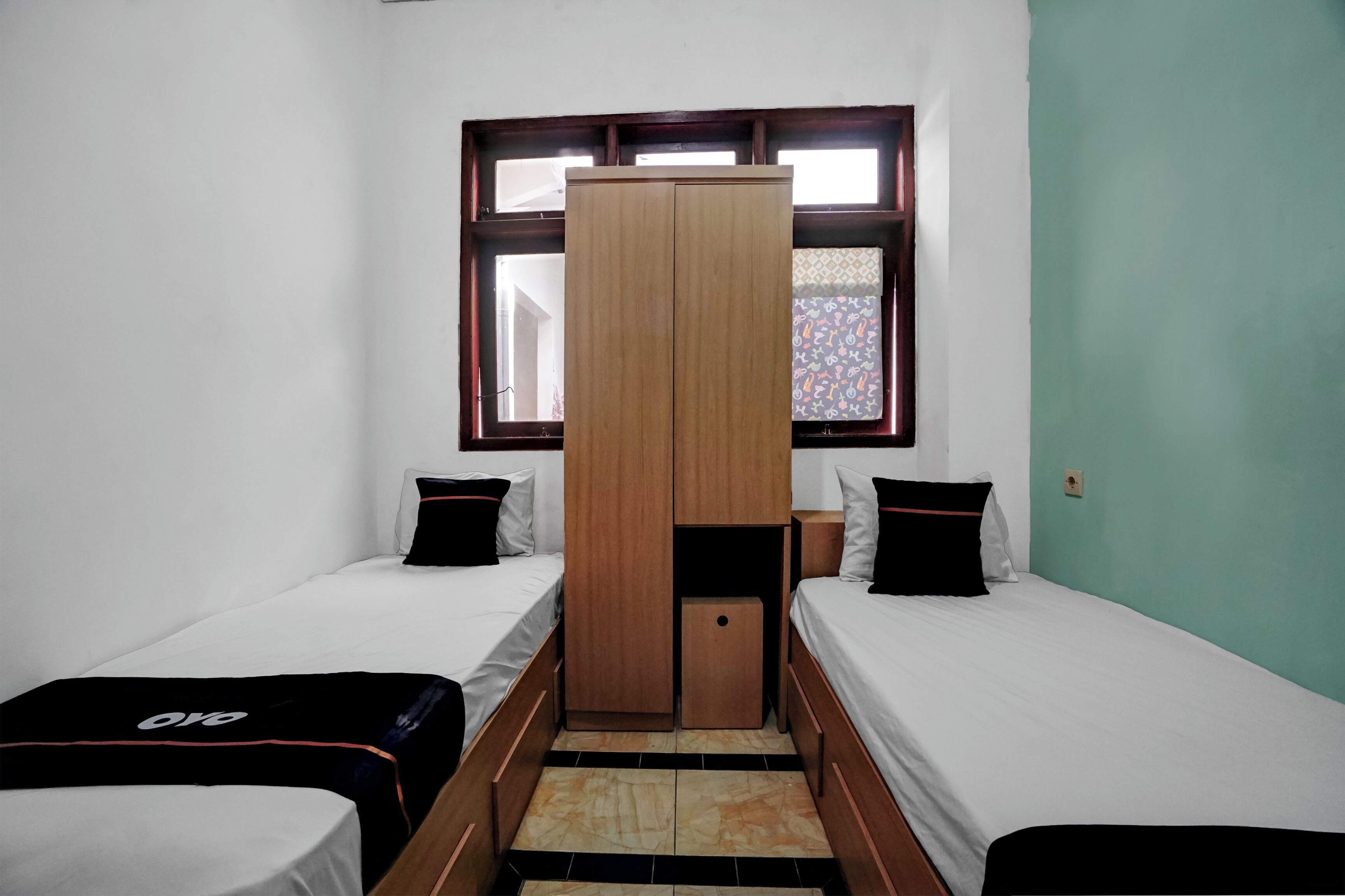 Une petite chambre compacte avec deux lits simples, une armoire et une fenêtre.