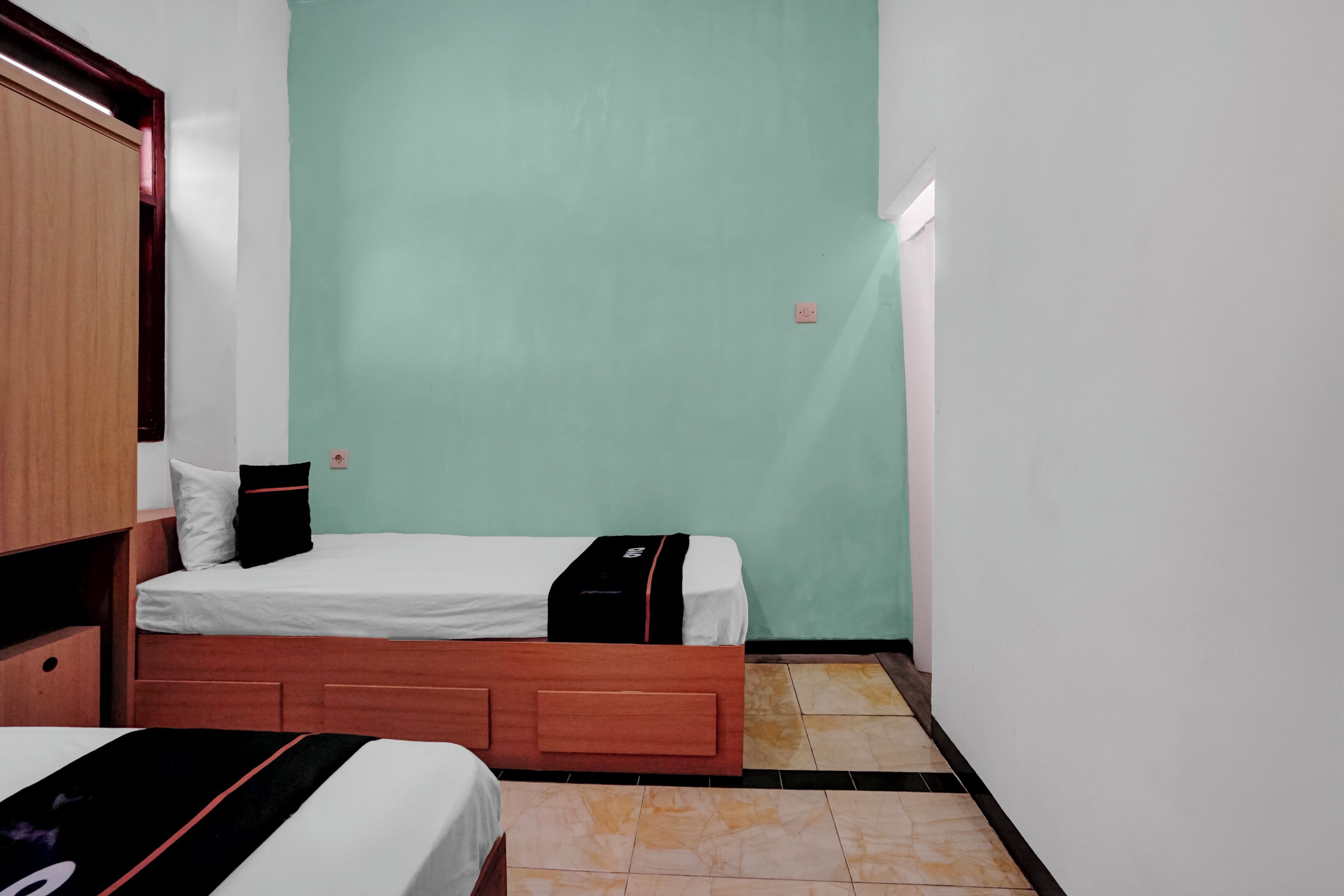A small, single-bed room with a wooden headboard, a white mattress, and a black and white blanket.