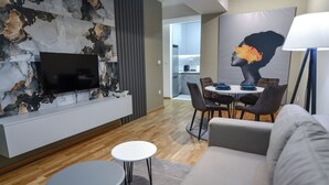 En moderne stue med et fladskærms-tv, et spisebord med stole, en sofa og en lampe.