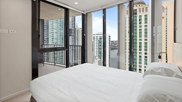 Ein modernes Hotelzimmer mit einem großen Bett, einer Schiebetür zu einem Balkon und Blick auf die Stadt.