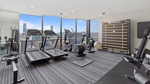 Ein modernes Fitnessstudio mit Laufbändern, Crosstrainern und Gewichtsgeräten, großen Fenstern mit Blick auf die Stadt und einer hohen Decke mit eingelassener Beleuchtung.