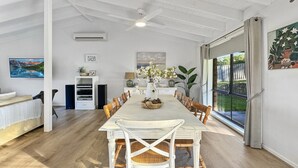 A spacious dining area with a long table, white chairs, and a ceiling fan. - Pet-friendly Private Retreat with Large Backyard (Surf Beach)