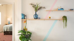 A room with a bed, a desk with a lamp, and a wall with shelves holding books, a vase, and a hanging plant. - Cosy 2-Bed Apartment in the Heart of Strathfield (Strathfield)