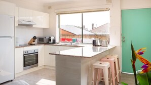 A modern kitchen with white cabinets, a built-in oven, a microwave, and a large window. - Cosy 2-Bed Apartment in the Heart of Strathfield (Strathfield)