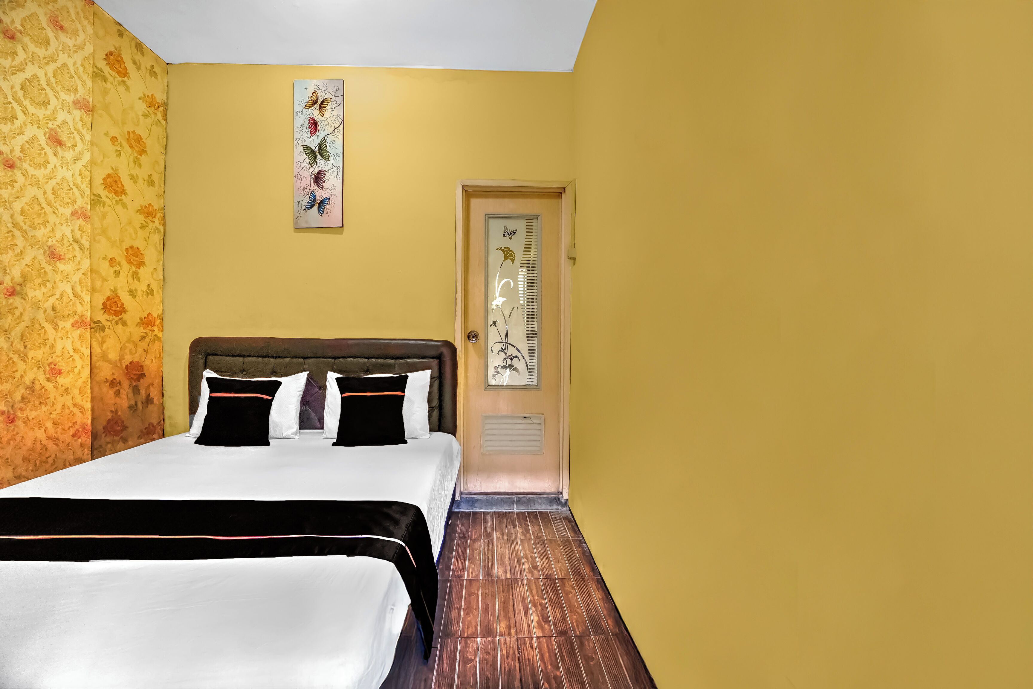 Una camera d'albergo con un letto, una testiera, una porta con una finestra e una parete con motivo floreale.