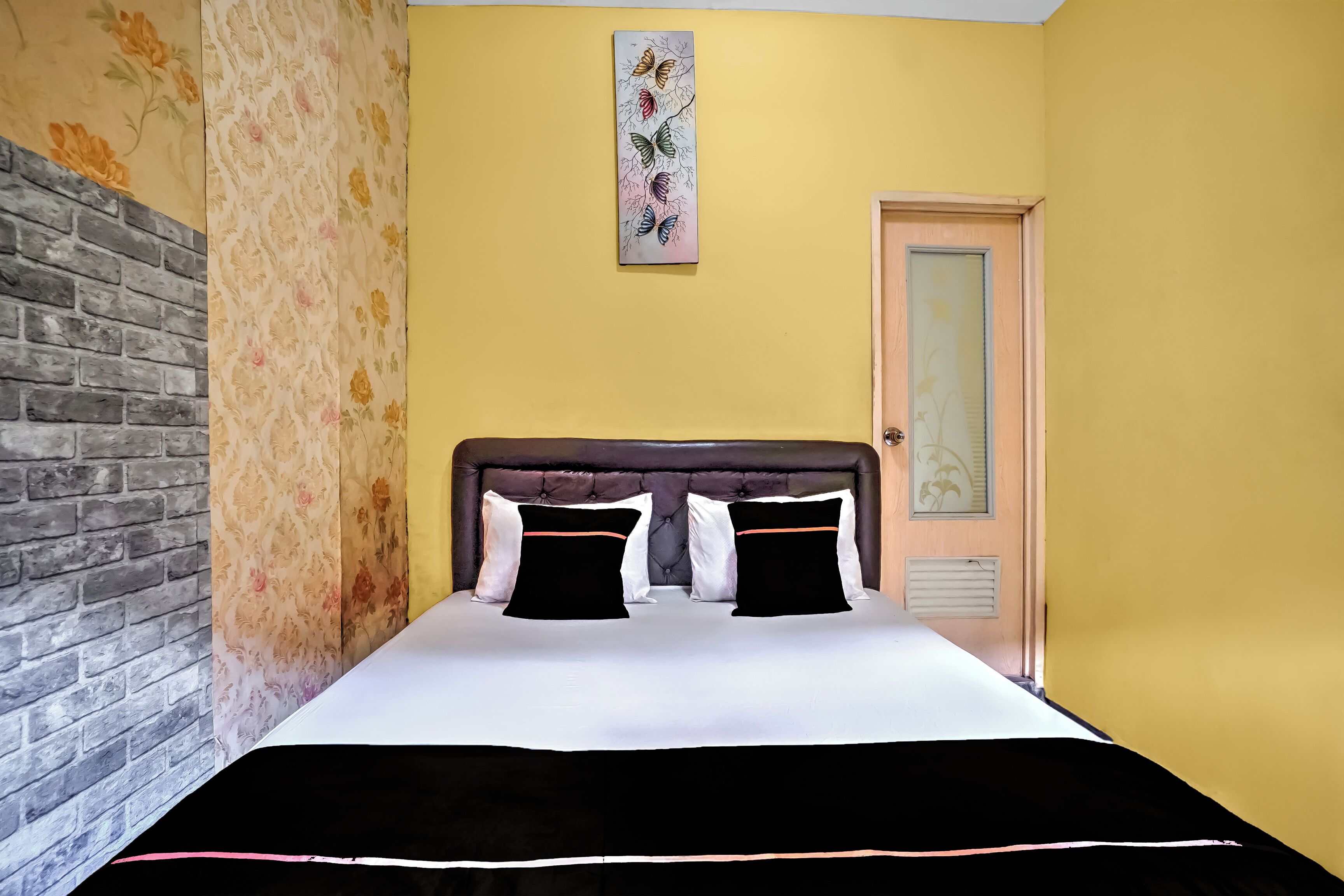 A bedroom with a brick wall, floral wallpaper, a bed with black and white bedding, and a painting of butterflies.