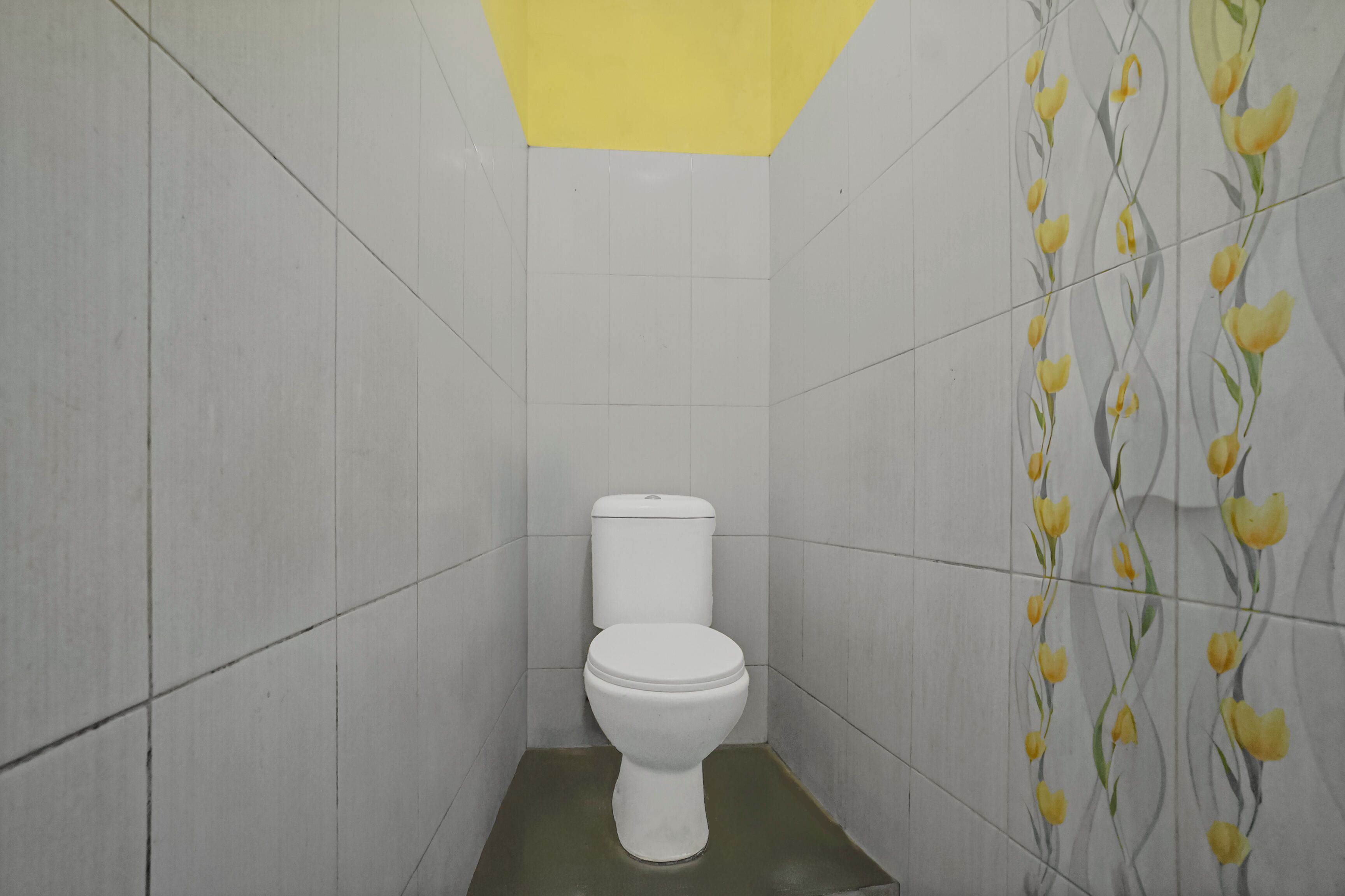 A small, compact bathroom with a white toilet, tiled walls, and a yellow ceiling.