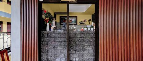 Entrada de un hotel con mostrador de recepción, un letrero que dice 'Welcome Reception' y una planta decorativa.