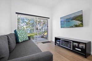 A modern living room with a grey sofa, a glass door leading to a balcony, and a black entertainment unit with media.