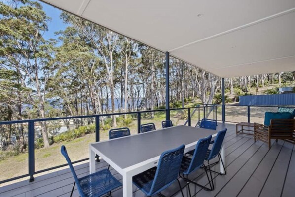 A covered outdoor area with a table and chairs, overlooking a forested area.