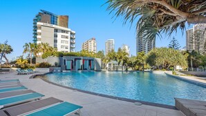 Una piscina con sillas de descanso, rodeada de palmeras y edificios modernos.
