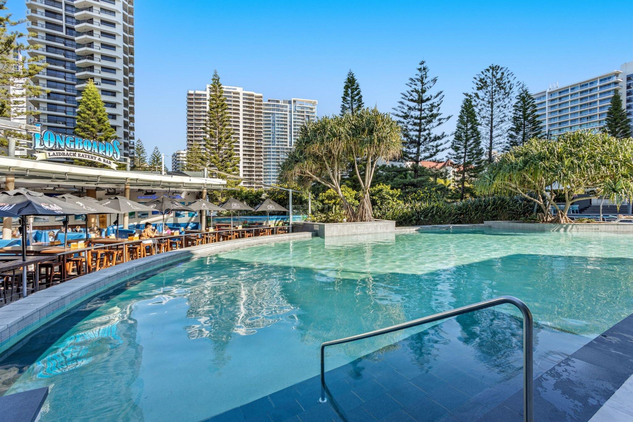 A swimming pool with a bar area, surrounded by trees and tall buildings.