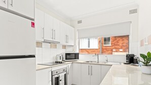 A modern kitchen with white cabinets, a microwave, a kettle, and a coffee machine. - Bright and convenient apartment, close to shops (Ryde)