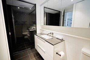 Ein modernes Badezimmer mit einer Duschkabine aus Glas, einem weißen Waschtisch mit Waschbecken und einem großen Spiegel darüber.