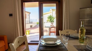 Un coin repas avec une table dressée pour deux personnes, une bouteille de vin et une vue sur la terrasse extérieure.