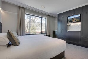 Quarto com uma cama grande, televisão fixada na parede e janela com cortinas.
