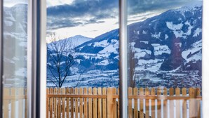 Une vue à travers une fenêtre, avec une clôture en bois, des montagnes enneigées et une ville en arrière-plan.