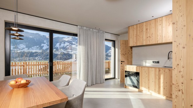 Une cuisine moderne avec des meubles en bois, un coin repas avec une table et des chaises, et une grande fenêtre offrant une vue sur les montagnes.