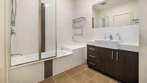 A modern bathroom with a glass-enclosed shower, a vanity with a mirror, and a dark wood cabinet. - Stunning 2-Bed Unit with BBQ Patio near Dining (Northcote)