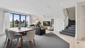 Una sala de estar moderna con comedor, ventanas amplias, una escalera y vistas de la ciudad.