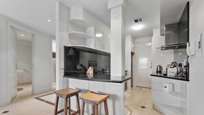 Una cocina moderna con armarios blancos, encimera negra y dos taburetes de madera.